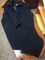 Black Linder size 16 coat with buttons laid on chair.