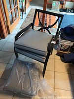 Stacked patio chairs showing gray cushions and black metal frames in an indoor setting.