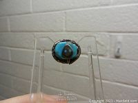 Front view of sterling silver and turquoise snake pin on clear display stand against white brick background