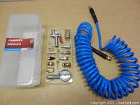 Overall view of coiled 25 ft air hose, plastic storage case, and accessory kit layout on table.
