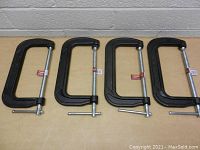 Four new 8 inch black Husky Heavy Duty C clamps arranged side by side on a wooden surface.