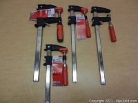 Four Bessey bar clamps laid out showing different sizes and black and red handles with product labels.
