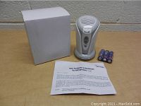 Photo showing the ionic freshener device, white packaging box, four AA batteries, and instruction sheet on a wooden surface.