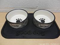 Front view of the two ceramic dog bowls labeled 'Food' and 'Water' on a black rubber mat with 'good dog' embossed.