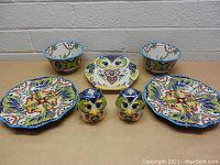 Overview of lot showing two large decorative plates, two matching bowls, one owl-shaped plate, and a pair of owl salt and pepper shakers arranged on a table.