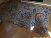 Full view of the rectangular area rug spread out on hardwood floor, showing overall multicolored floral design.