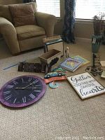 Wide view showing the clock on carpet, metal key rack to right, wall art signs with quotes, blue-green vase beside a bird figurine on the floor, two menorahs visible in background, small decorative boxes