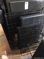 Folded large and medium size black metal wire dog crates with plastic bottoms stacked upright.