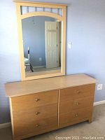 Photo shows the light wood six drawer dresser with a rectangular wood-framed wall mirror attached above it. Mirror has an arch and slats decoration.