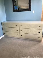 Front view of white dresser with six drawers, visible drawer knobs, placed against a blue wall on carpet.