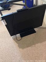 Side front view of Dynex 32 inch flat screen television on stand, showing screen and wiring.