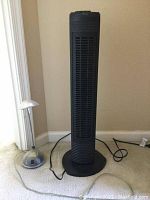 Wide view of both items: silver adjustable desk lamp and black Holmes tower fan on carpet floor