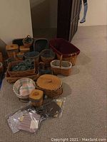 Photo showing an assortment of woven Longaberger baskets of varying sizes, some with lids and fabric liners inside. Baskets are natural wood tone and some have dark brown or red woven accents.
