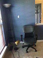 Adjustable office chair with armrests between a tall floor lamp with frosted glass shade and a smaller gold desk lamp with frosted glass shade