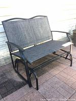 Full front view of the patio glider showing seat, backrest, armrests, and metal frame.