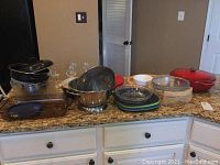 Full lot overview showing the red cast iron pot, multiple glass baking dishes, clear glass bowls, melamine plates, ceramic bowls including the chipped Gibson bowl, and stemware