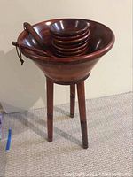 Large wooden salad bowl on a tripod wooden stand, holding 8 small wooden salad bowls and a pair of wooden tongs inside large bowl.