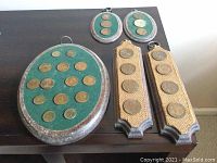 Five wood plaques with mounted vintage coins in various shapes and fabric colors placed on table surface.