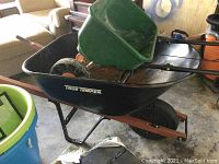 View of Scotts Speedy Green 3000 spreader on top of True Temper wheelbarrow in storage area.