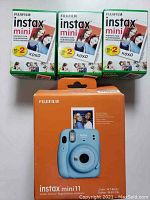 Three boxes of Fujifilm instax mini instant film and boxed Fujifilm instax mini 11 instant camera in sky blue.