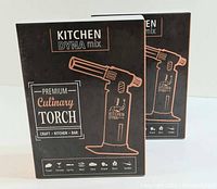 Two boxed DYNA mix Premium Culinary Torches, black and copper color scheme, shown front view of packaging.