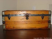 Front view of the antique chest showing the pine wood construction with metal banding and central lock with clasps.