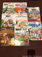 Eight Asterix paperback graphic novels arranged on a surface, front covers visible with colorful illustrations and titles.
