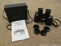 Binoculars with case, instruction booklet, and lens caps displayed on carpeted floor