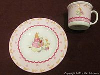 Photo showing the plate and mug on a dark surface with the bunny and heart designs visible, plate on left and mug on right