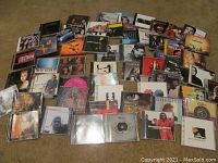 Photo showing a large assortment of CD jewel cases spread over carpeted floor with visible album covers