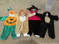 All four children's Halloween costumes laid flat on carpet: pumpkin, lion, witch, and bear.