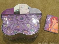 Top view of transparent purple flower-shaped plastic container with 24 assorted charms inside compartments, sealed in original plastic.