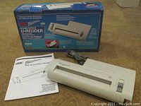 GBC Shredmaster 60S shredder in beige placed on carpet floor with original blue box and manual, showing full unit with power cord.