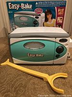 Front view of Easy-Bake Oven with original box in background and yellow pan tool in front