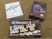 Lot photo showing boxed Sequence, Code Breaker, and Rummikub games on carpeted floor.