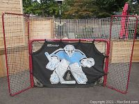 Front view of red frame hockey net with attached shooter tutor panel showing goalie image, puck collector pockets, and extended safety netting on top and sides.