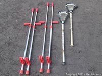 Two pairs of B+oco adjustable stilts with red grips next to two Barracuda lacrosse sticks on ground.