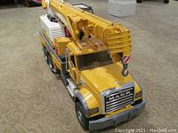 Front perspective of yellow Mack Liebherr crane truck toy showing the cab with Mack logo, front grill, and crane arm stowed position.