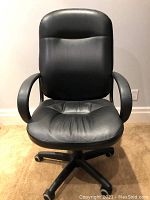 Front view of black leather office chair showing padded seat and backrest, armrests, and five-wheel base.