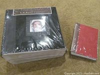 Photo showing three large photo albums in plastic wrap and one small red photo album placed on the floor.