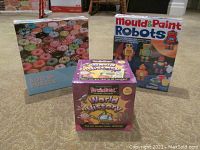 Lot overview showing three items: Cobble Hill 500 piece donut puzzle box, Mould & Paint Robots kit box, and BrainBox World History game box, all arranged on floor.