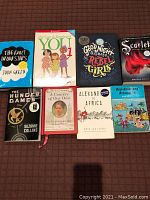 Top view of 8 books arranged on a brown surface showcasing front covers including 'The Fault in Our Stars', 'Good Night Stories for Rebel Girls', 'Scarlette', and others.