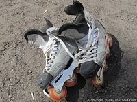 Pair of silver and black Vector PF6 inline rollerblades with orange wheels on pavement.