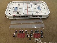 Overhead view of the full Stiga table hockey game with disassembled clear plastic endglass pieces and 3D blue and white hockey player figures with red goals on a brown carpet.