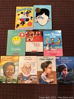 Top-down image of the 9 books arranged on a brown surface showing their front covers, including graphic novels, biographical books, and novels.