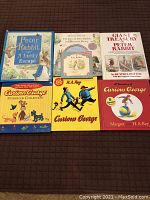 Overview photo showing 7 books including Peter Rabbit titles and Curious George story collections spread on a surface.