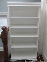 Front view of white painted wooden bookshelf showing four shelves and top moulding detail.