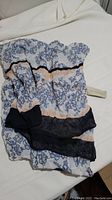Floral print scarf partially folded showing light blue flowers with black and peach color banding, with tag visible.