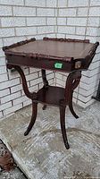 Full image of dark wood antique side table with curved legs, lower shelf and lion head carvings on corners
