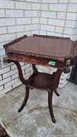 Full view of the antique wooden side table with carved lion heads and lower shelf.